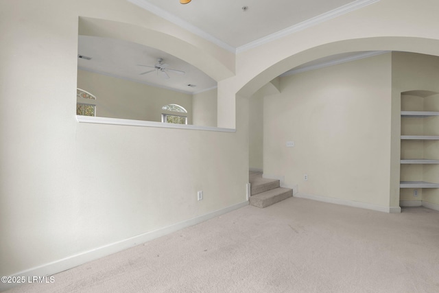 carpeted empty room with crown molding, built in shelves, a ceiling fan, and baseboards