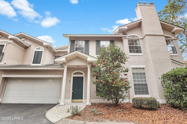 townhome / multi-family property featuring aphalt driveway, a chimney, an attached garage, and stucco siding