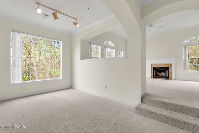 carpeted living room with a wealth of natural light, rail lighting, visible vents, a ceiling fan, and ornamental molding