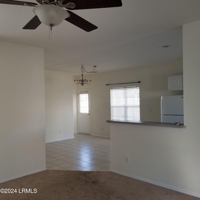 tiled spare room featuring ceiling fan with notable chandelier