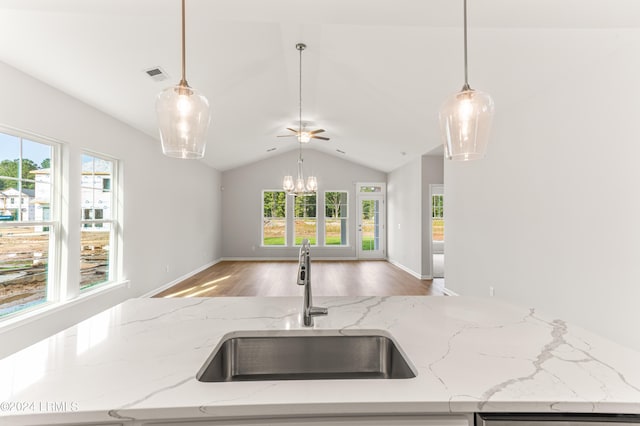 kitchen featuring pendant lighting, sink, wood-type flooring, light stone countertops, and vaulted ceiling