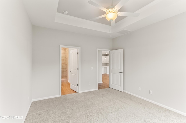 unfurnished bedroom featuring a raised ceiling, light carpet, ceiling fan, and ensuite bath