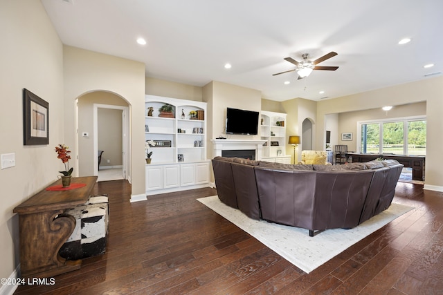 living room with built in shelves, ceiling fan, and dark hardwood / wood-style flooring