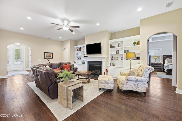 living room with built in features, dark hardwood / wood-style floors, and ceiling fan