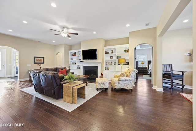 living room with built in shelves, ceiling fan, and dark hardwood / wood-style flooring