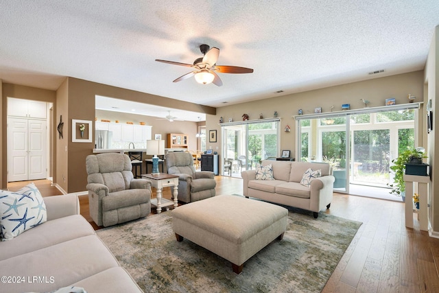 living room with wood-type flooring, ceiling fan, and a textured ceiling