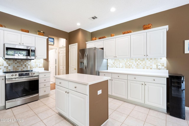 kitchen with a kitchen island, appliances with stainless steel finishes, light tile patterned floors, and white cabinets