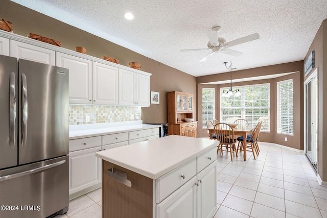 kitchen featuring white cabinetry, a textured ceiling, stainless steel fridge, a kitchen island, and backsplash