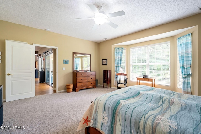 carpeted bedroom featuring a textured ceiling, a walk in closet, a closet, and ceiling fan