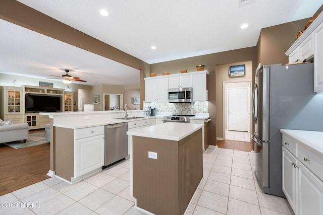 kitchen featuring stainless steel appliances, a center island, white cabinets, light tile patterned flooring, and kitchen peninsula