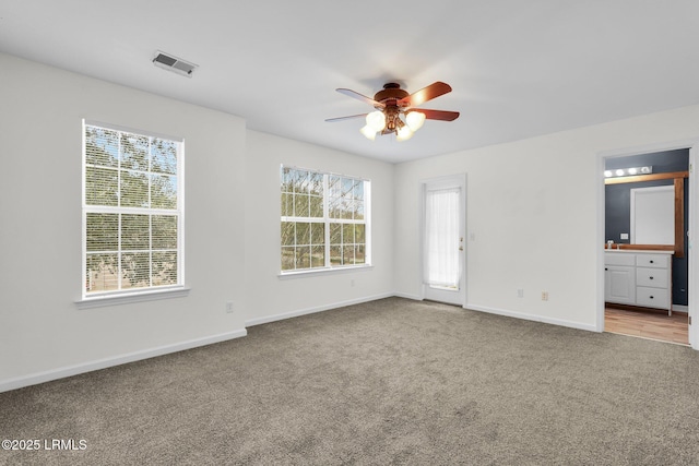 unfurnished bedroom with multiple windows, ensuite bathroom, light colored carpet, and ceiling fan