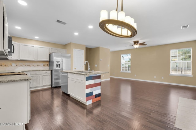 kitchen with stainless steel appliances, white cabinets, backsplash, and decorative light fixtures