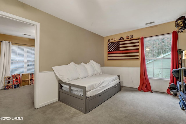 carpeted bedroom with visible vents and a wainscoted wall