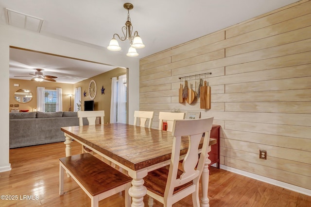 dining room featuring ceiling fan with notable chandelier, wooden walls, light wood-style floors, and visible vents