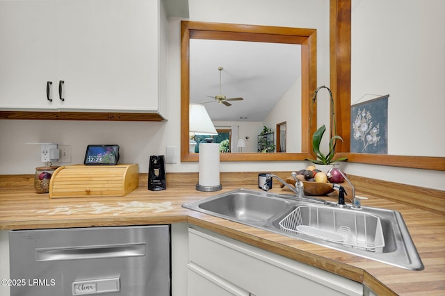 kitchen with butcher block countertops, a ceiling fan, a sink, stainless steel dishwasher, and white cabinets