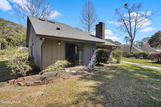 back of house featuring a lawn, roof with shingles, and a chimney