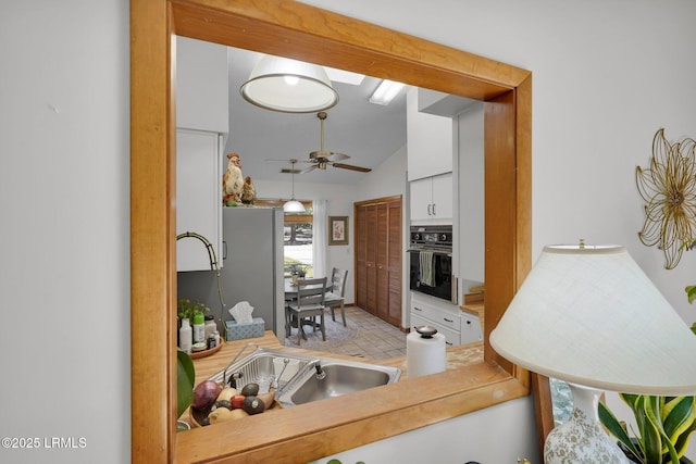 kitchen featuring oven, lofted ceiling, hanging light fixtures, white cabinetry, and a ceiling fan