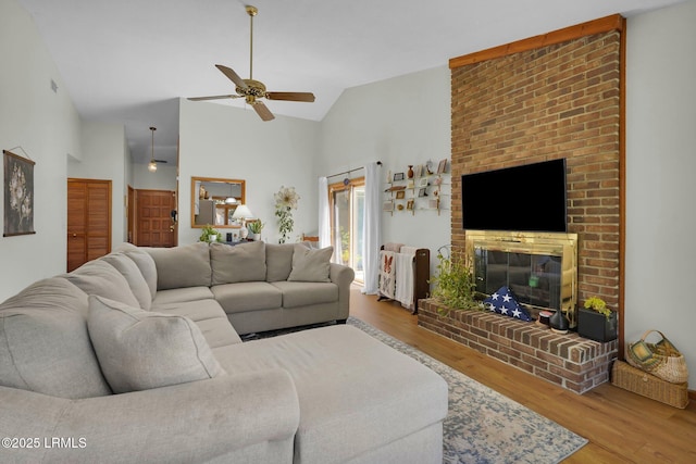 living area with ceiling fan, a brick fireplace, wood finished floors, and high vaulted ceiling