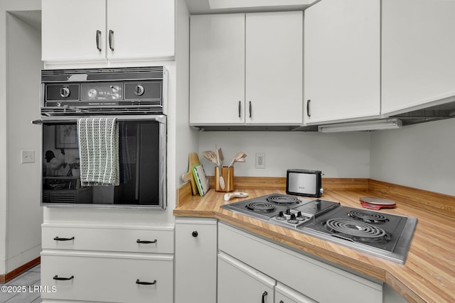 kitchen featuring oven, stainless steel electric stovetop, and white cabinetry