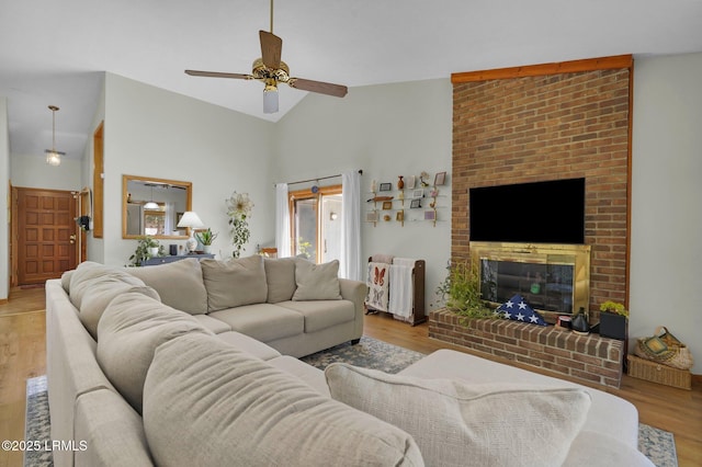 living area with high vaulted ceiling, a brick fireplace, light wood-style flooring, and a ceiling fan