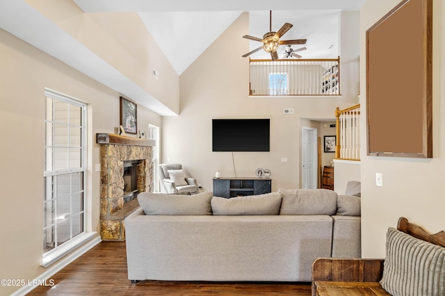 living room with visible vents, a ceiling fan, dark wood-style flooring, a stone fireplace, and high vaulted ceiling