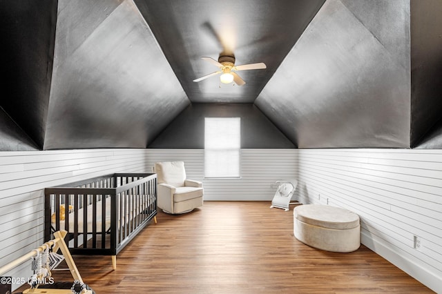 additional living space with vaulted ceiling, wood walls, wood finished floors, and a ceiling fan