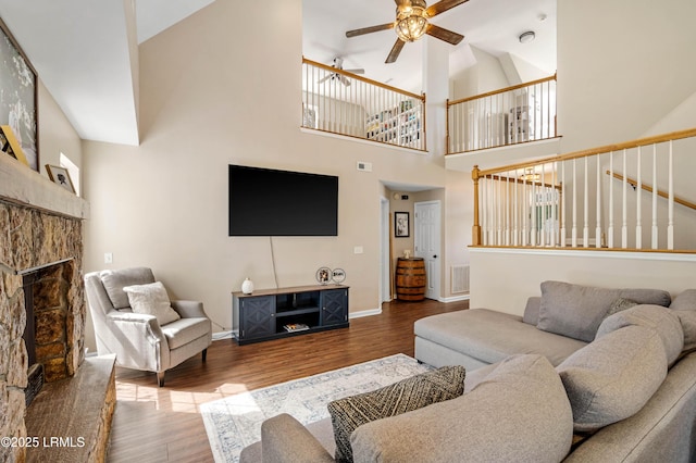 living room with a fireplace with raised hearth, ceiling fan, wood finished floors, and baseboards