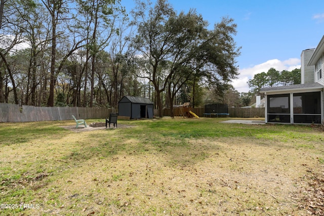 view of yard with a trampoline, an outbuilding, a storage shed, a sunroom, and a fenced backyard