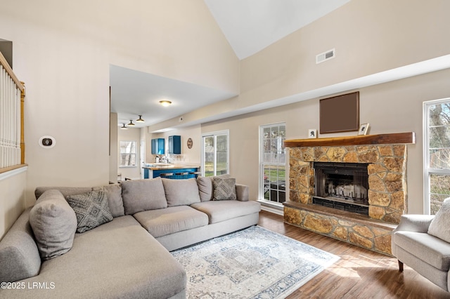 living area featuring high vaulted ceiling, a fireplace, visible vents, and wood finished floors