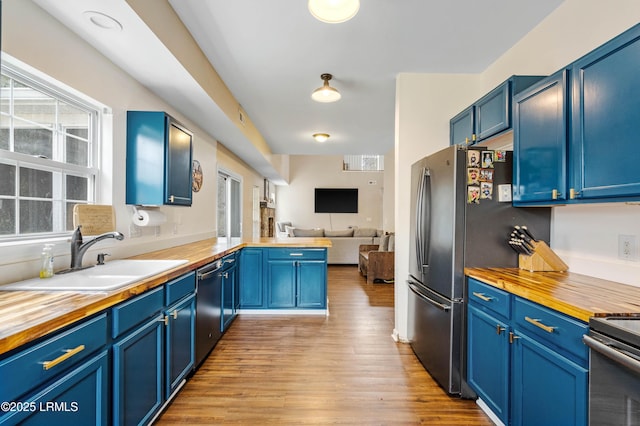 kitchen featuring blue cabinetry, butcher block countertops, open floor plan, and a sink