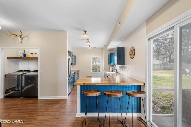 kitchen featuring blue cabinetry, a breakfast bar area, dark wood-type flooring, freestanding refrigerator, and washer and dryer