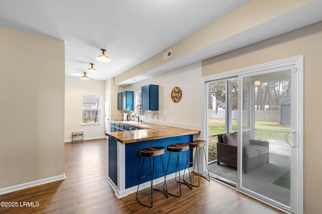 kitchen with visible vents, a kitchen breakfast bar, wooden counters, blue cabinetry, and dark wood-style floors