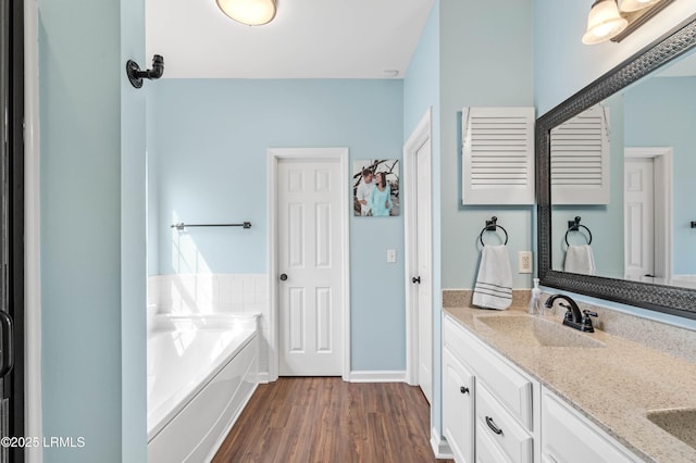 bathroom with a bath, double vanity, a sink, and wood finished floors