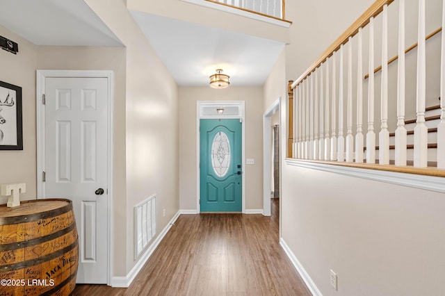 foyer entrance with baseboards, stairs, visible vents, and wood finished floors