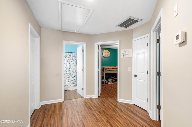 corridor featuring attic access, visible vents, baseboards, and wood finished floors