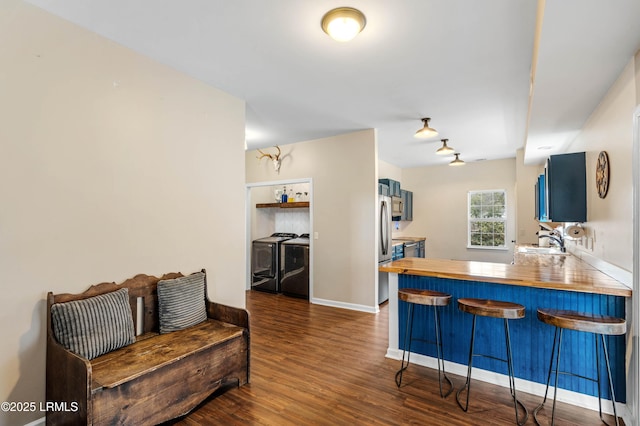 kitchen with blue cabinets, a breakfast bar, dark wood-type flooring, a sink, and washing machine and clothes dryer