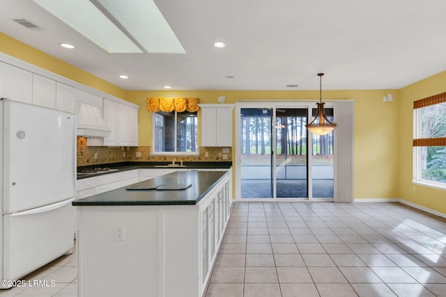 kitchen with tasteful backsplash, white cabinets, dark countertops, freestanding refrigerator, and stainless steel gas stovetop