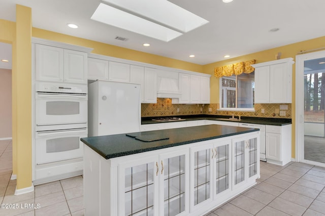 kitchen featuring dark countertops, double oven, white cabinetry, and a center island