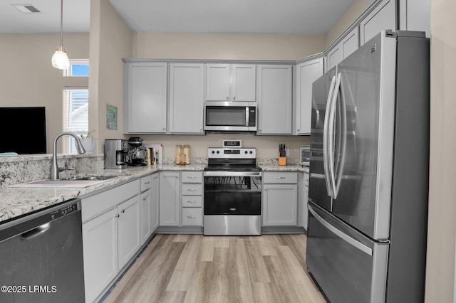 kitchen with decorative light fixtures, sink, light stone counters, stainless steel appliances, and light hardwood / wood-style flooring