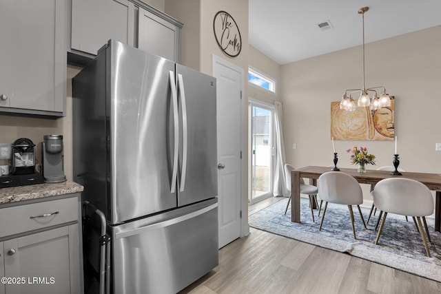 kitchen featuring gray cabinets, hanging light fixtures, stainless steel fridge, and light hardwood / wood-style flooring