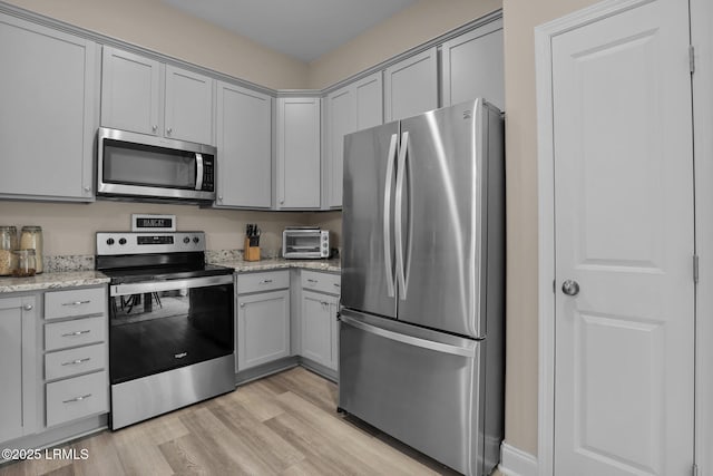 kitchen featuring light stone counters, stainless steel appliances, gray cabinets, and light hardwood / wood-style flooring