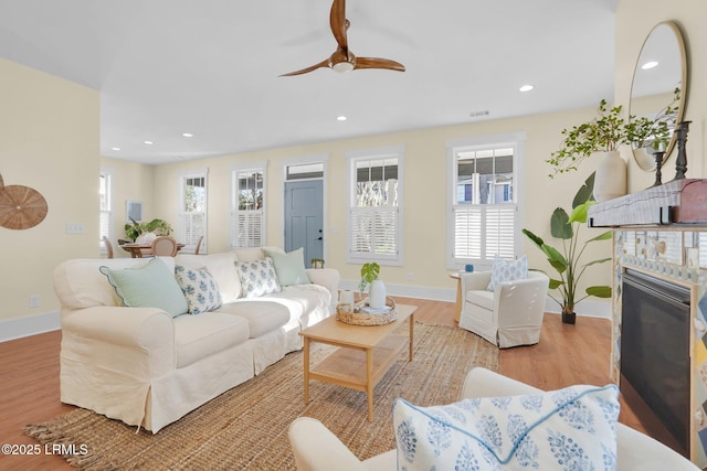 living area with a glass covered fireplace, baseboards, recessed lighting, and wood finished floors