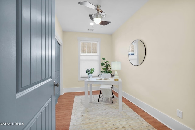 office space with a ceiling fan, visible vents, baseboards, and wood finished floors