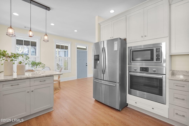 kitchen featuring appliances with stainless steel finishes, light stone counters, hanging light fixtures, light wood-style floors, and recessed lighting