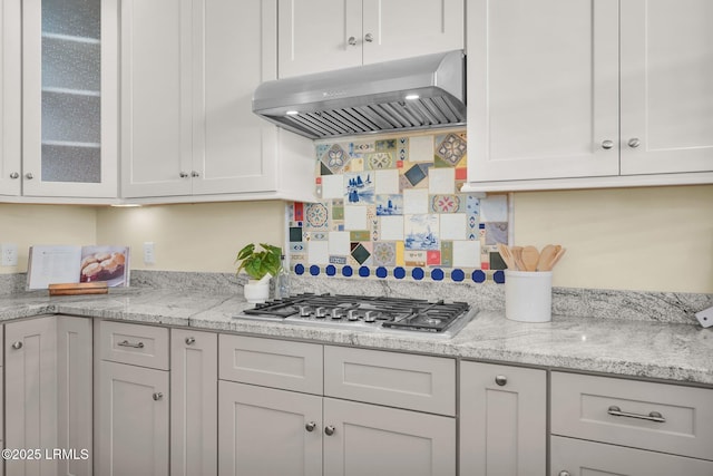 kitchen featuring white cabinetry, wall chimney exhaust hood, tasteful backsplash, glass insert cabinets, and stainless steel gas stovetop