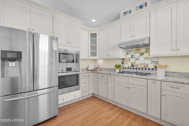 kitchen with stainless steel appliances, light wood-style flooring, glass insert cabinets, white cabinetry, and under cabinet range hood