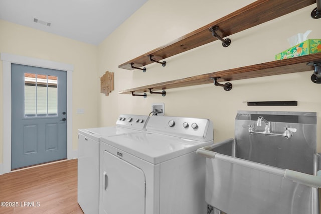 clothes washing area with laundry area, light wood-style flooring, washer and clothes dryer, and a sink