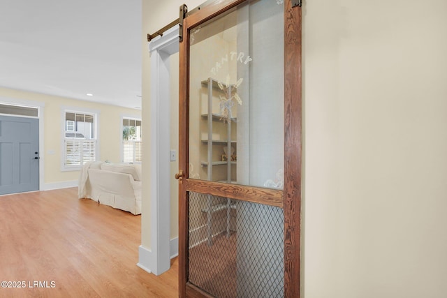 hall with light wood-type flooring, a barn door, and baseboards