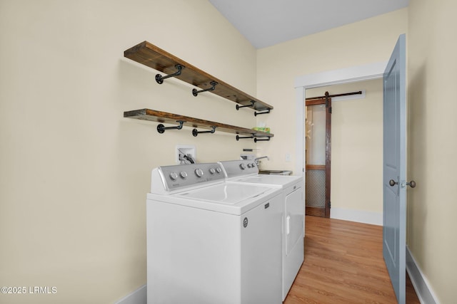 clothes washing area with a barn door, laundry area, baseboards, light wood-style floors, and washing machine and clothes dryer