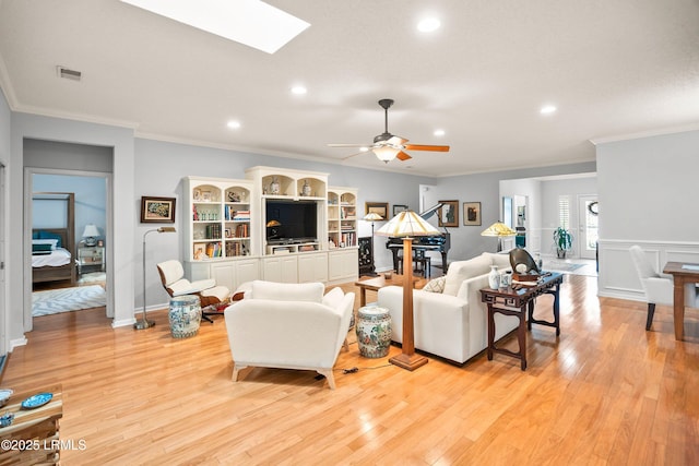 living room with crown molding, a skylight, and light hardwood / wood-style floors